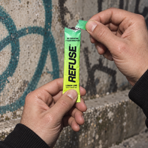 Two hands tearing the top off a REFUSE lemon lime stick pack